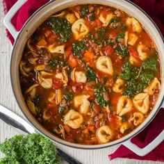 a pot filled with pasta and spinach soup on top of a red cloth next to a spoon