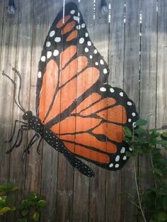 an orange and black butterfly painted on the side of a wooden fence with white dots