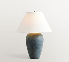 a blue vase with a white shade on it sitting next to a light that is turned on