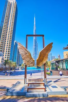 an angel statue in front of the burj building and skyscrapers, kuwait