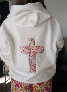 a woman wearing a white hoodie with a cross on it's chest and floral print pants