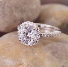 a white diamond ring sitting on top of a rock with rocks in the back ground