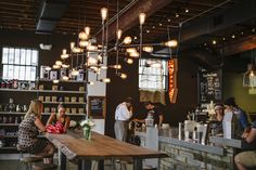 people sitting at tables in a restaurant with lights hanging from the ceiling