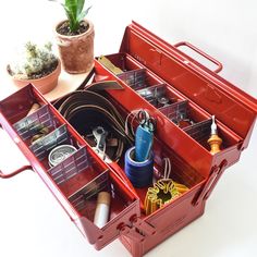 a red toolbox filled with lots of tools and other items next to a potted plant