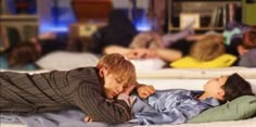 two children laying on top of each other in a room full of people and books