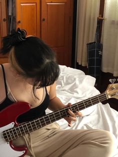 a woman sitting on top of a bed holding a red guitar