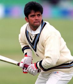 a man holding a cricket bat on top of a green grass covered field with spectators in the background