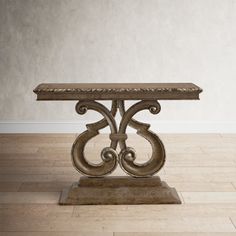 an ornate table with marble top on a wooden floor in front of a white wall