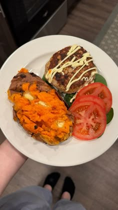 a person holding a white plate with some food on it and a burger, tomatoes, and lettuce