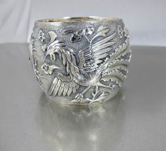 Fabulous beautifully detailed antique Qing Dynasty Chinese wide Sterling Silver bangle Bracelet with raised image of a Phoenix and a Dragon with what looks like the Sun at the center.  According to the hallmark CHINA 100 23 this piece is mid19th century and may have been one of a pair of Wedding Bracelets.  The Dragon represents the Masculine with its strength and power, while the Phoenix embodies the feminine, representing grace and beauty.  Together they signify the harmonious union of opposites. A stunning piece that will become a family heirloom for many years to come. A wonderful addition to your antique jewelry collection! Bracelet is in great condition. Opens and closes securely.  Hallmarked CHINA 100 23. Measures 2.25 inches from top to bottom and the inside measures 6.50 inches ar Victorian Bangle With Intricate Design For Ceremonial Occasions, Antique Round Cuff Bracelet For Wedding, Victorian Engraved Cuff Bracelet For Ceremonial Occasion, Antique Hallmarked Bangle For Weddings, Antique Etched Bangle For Wedding, Antique Etched Bracelets For Wedding, Antique Etched Wedding Bangle, Victorian Style Ceremonial Cuff Bracelet With Intricate Design, Victorian Cuff Bracelet With Intricate Design For Ceremonial Occasions