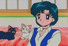 a woman holding a cat in front of her and another cat sitting on the bed behind her