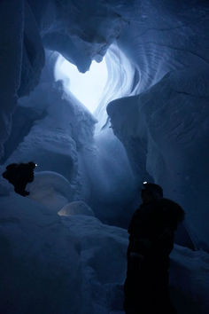 two people are standing in the middle of a narrow ice cave with light coming through