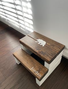 a wooden step stool sitting on top of a hard wood floor next to a window