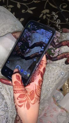 a woman holding up her phone with henna on it