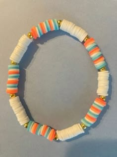 an orange, white and blue beaded bracelet with gold beads on a gray surface