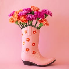 On a pink background is a pink cowboy boot shaped vase with a red and white daisy print on it. Flowers pictured not included with purchase. Disco Cowboy Home Decor, Western Arts And Crafts, Valentine’s Day Decor For Office, Pink Gumball Machine, Cowboy Boot Flower Vase, Disco Cowboy Decor, Valentines Apartment Decor, Disco Cowgirl Room Decor, Ceramic Cowboy Boot