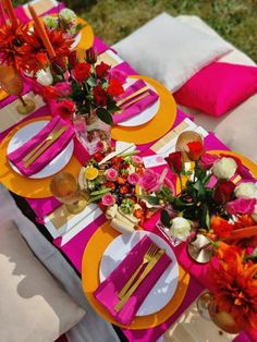 the table is set with pink and yellow plates, silverware, and colorful flowers