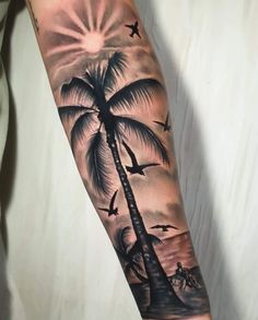 a man's arm with a palm tree and birds on it, while the sun is setting