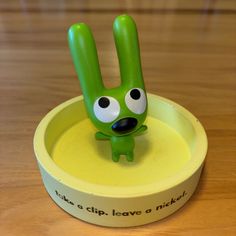 a green toy in the shape of a peace sign with eyes and hands sticking out