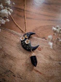 a necklace with a black moon and white flowers hanging from it's side on a wooden surface