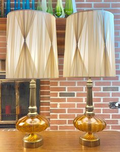 two lamps sitting on top of a wooden table next to a brick wall and fireplace