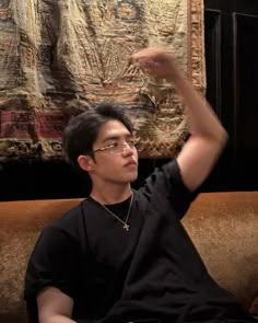 a young man sitting on top of a brown couch next to a wall hanging tapestry