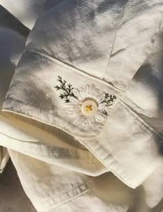 a white shirt with embroidered flowers on the front and back buttons is laying down in the sun