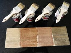 four paint brushes and three different shades of brown on a black table with wood samples