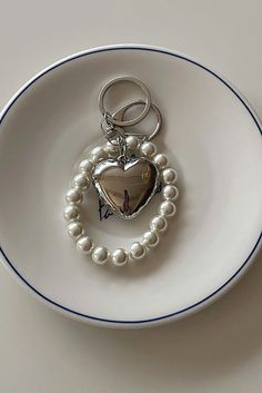 a white plate with a heart shaped keychain and pearls on the edge, sitting on a table