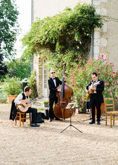 three men playing instruments in front of a house