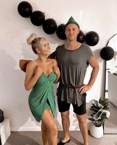 a man standing next to a woman in a green dress and black balloons on the wall