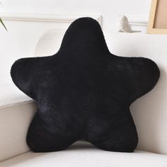 a black star shaped pillow sitting on top of a white couch next to a plant