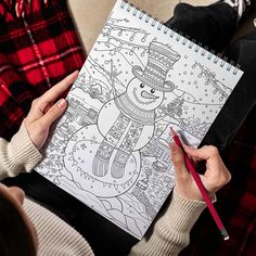 a person holding a coloring book with a snowman on it and a red pencil in their hand