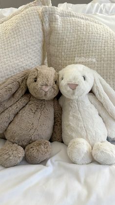 two stuffed animals sitting on top of a bed next to each other, one is hugging the other