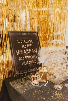 a welcome sign on a black table with gold streamers behind it and champagne glasses