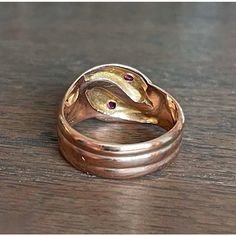 In the quiet, storied streets of Birmingham, 1918—a city teeming with industrious spirit and the echoes of a bygone era—a master goldsmith crafted this splendid creation. With its serpentine elegance, this ring features two serpents entwined in a dance of eternal allure. Each snake, rendered in lustrous 9 karat gold, showcases the hallmark of an era: the anchor for Birmingham and the letter 'T' denoting the year 1918, alongside the revered maker’s mark ‘H.W. Ld’. These symbols of authenticity promise not just a piece of jewelry, but a journey through time.  Adorning each serpent's head is a resplendent fuchsia-colored round faceted ruby measuring 2.6 mm across. These radiant gemstones capture the essence of a captivating twilight and reflect a world where opulence meets the extraordinary. Antique Hallmarked Snake Ring, Vintage Hand Forged Yellow Gold Rings, Antique Hand Forged Rings For Formal Occasion, Antique 14k Gold Snake Ring Gift, Antique 14k Gold Snake Ring For Anniversary, Vintage 14k Gold Snake Ring, Vintage 14k Yellow Gold Snake Ring, Vintage 14k Gold Snake Ring As A Gift, Antique Gold Snake Ring For Formal Occasions