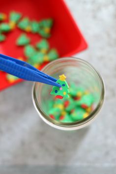 a glass jar filled with green and yellow frosting next to a red tray full of decorated cookies