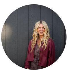 a woman with blonde hair standing in front of a black wall wearing a red jacket