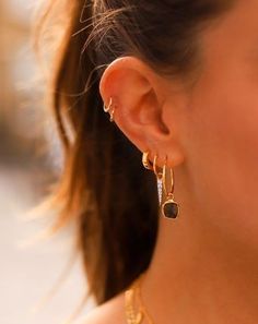 a close up of a woman's ear wearing gold earrings and a black necklace