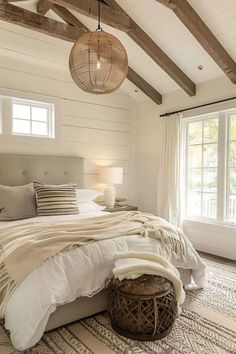 a large bed in a bedroom with white walls and wood beams on the ceiling, along with two windows