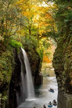 people are in boats near a waterfall and some trees with yellow leaves on the ground