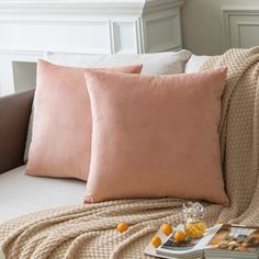 two peach colored pillows sitting on top of a couch next to a book and oranges