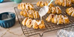 a spoon drizzling icing onto some pastries on a cooling rack