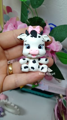 a hand holding a small white and black cow figurine on it's finger