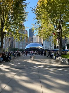 people are sitting on benches in the middle of an open area with trees and buildings behind them