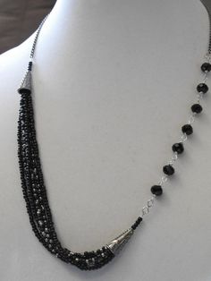 Fun black and silver crystal and seed bead necklace. The necklace measures 25 long and has a lobster clasp closer. It is made up of 6 strands of seed beads with decorative cone bead caps on the right and has black rondelle crystals on the left. This necklace would look great with a pair of jeans or Silver Multi-strand Beaded Necklace With Black Beads, Black Multi-strand Necklace With Silver Beads, Black Multi-strand Necklace With Faceted Beads, Black Beaded Necklaces With Lobster Clasp, Black Onyx Beaded Necklace With Faceted Beads, Silver Onyx Beaded Necklace With Black Beads, Asymmetrical Jewelry, Czech Beads Jewelry, Beaded Things