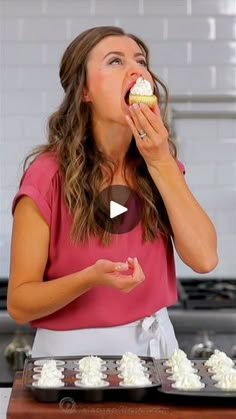 a woman in a pink shirt is eating a cupcake with white frosting on it