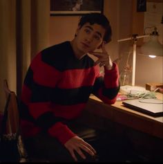 a young man sitting at a desk in front of a lamp