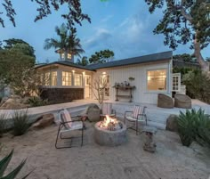 a fire pit sitting in the middle of a sandy area next to a white house