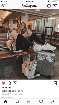 a woman sitting on top of a wooden bench next to an airport luggage bag and suitcase